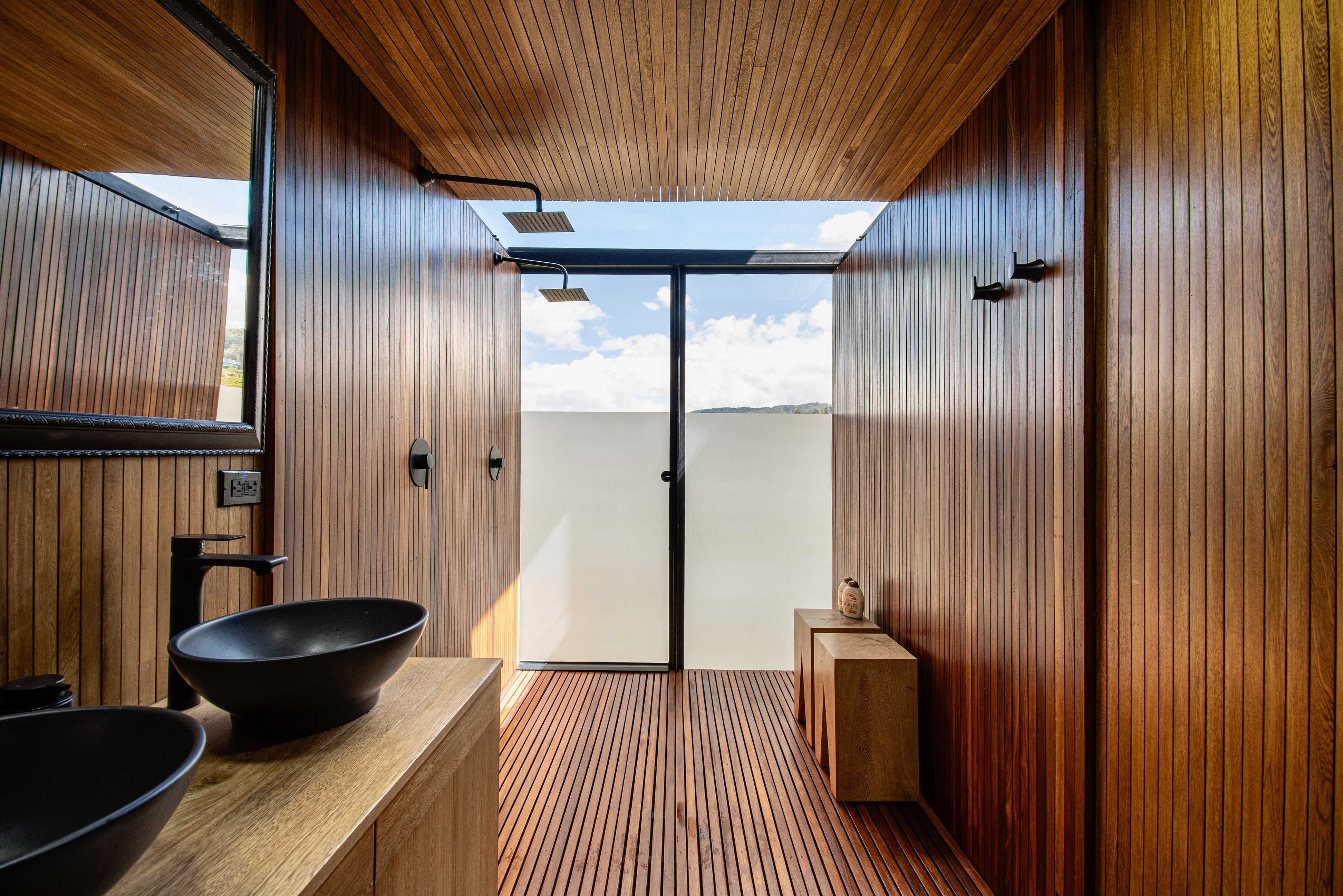 Wood-lined bathroom with a black basin and glazed shower