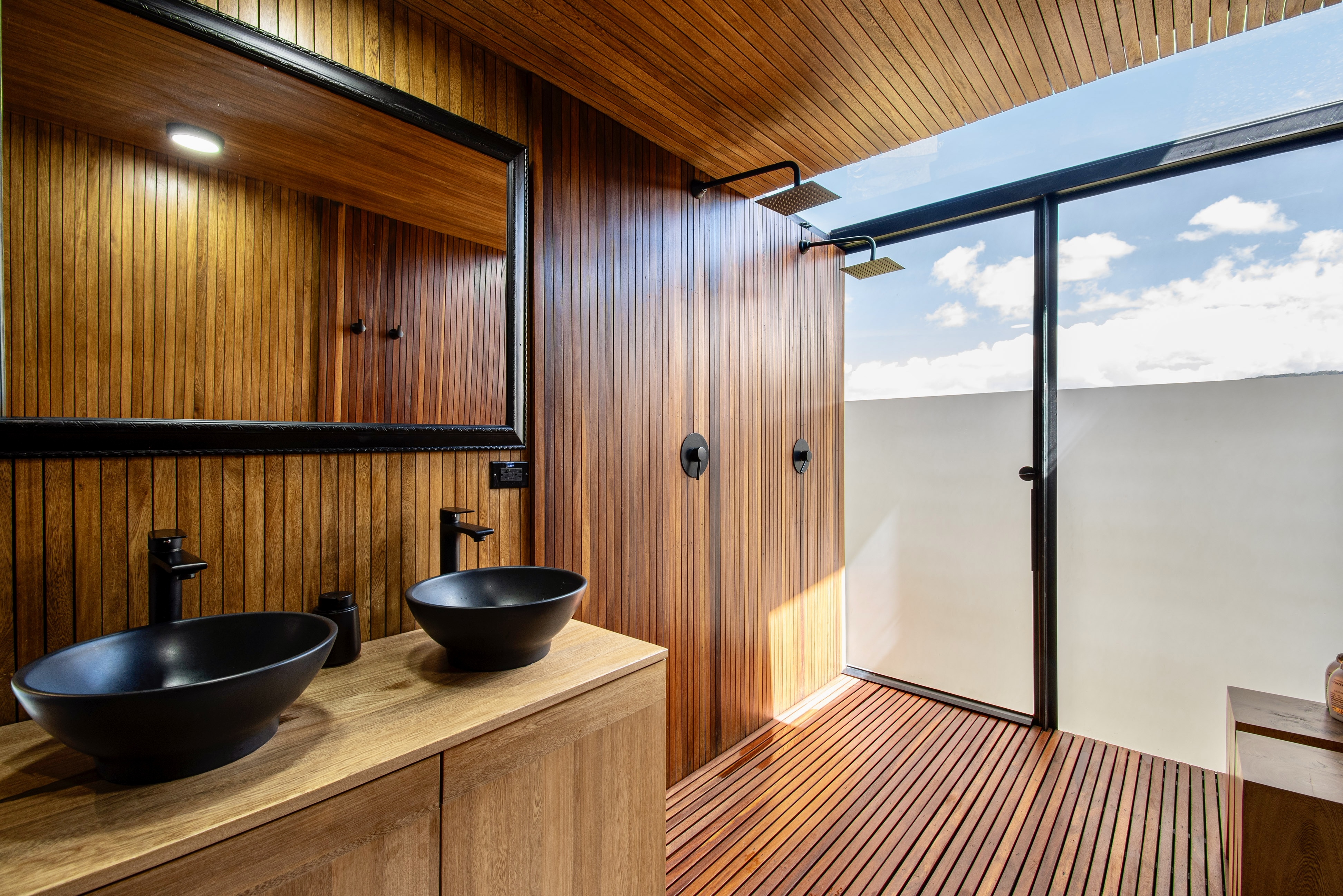 Bathroom vanity with two black basins beside a glazed shower