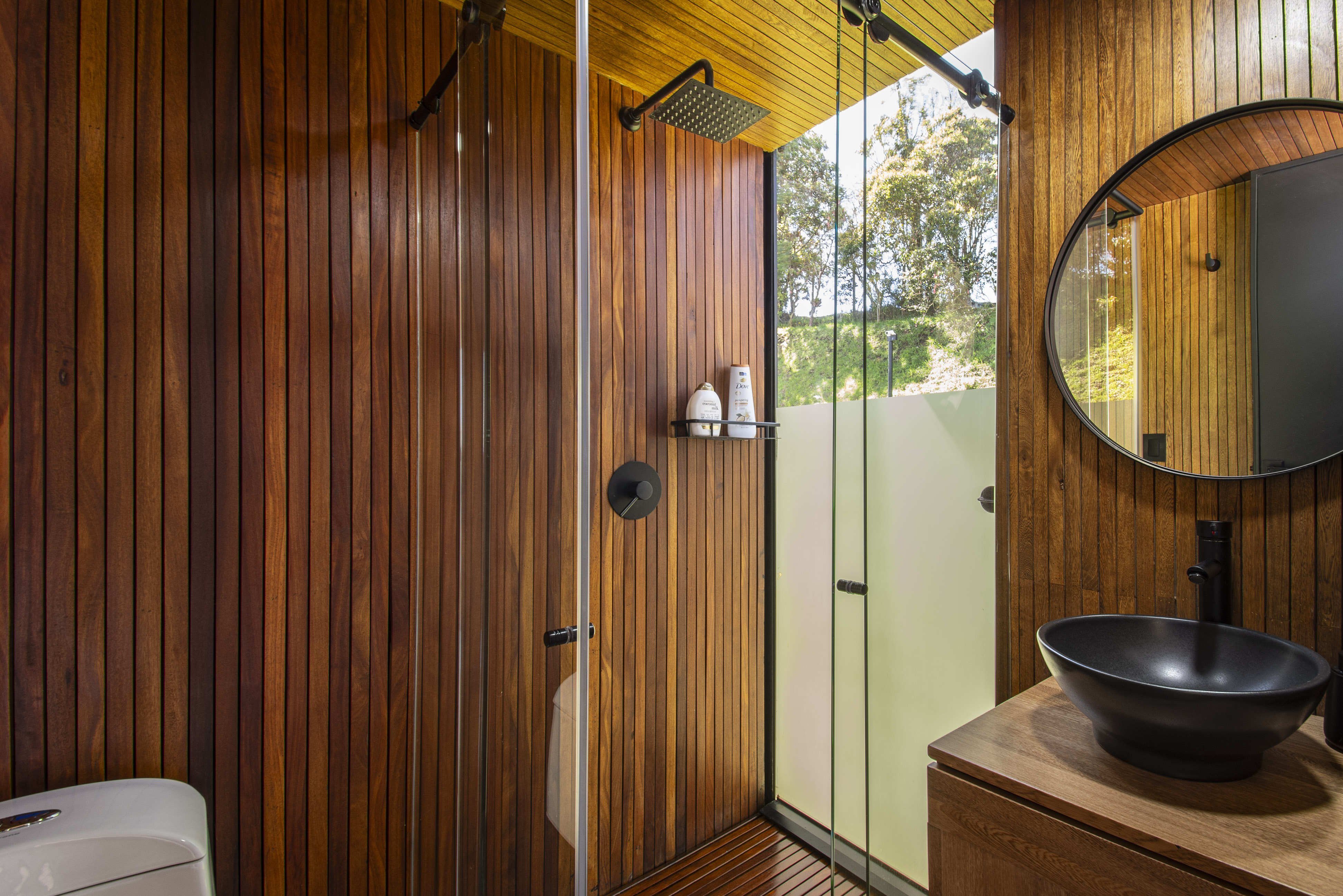 Wood-lined bathroom with a round mirror and glazed shower