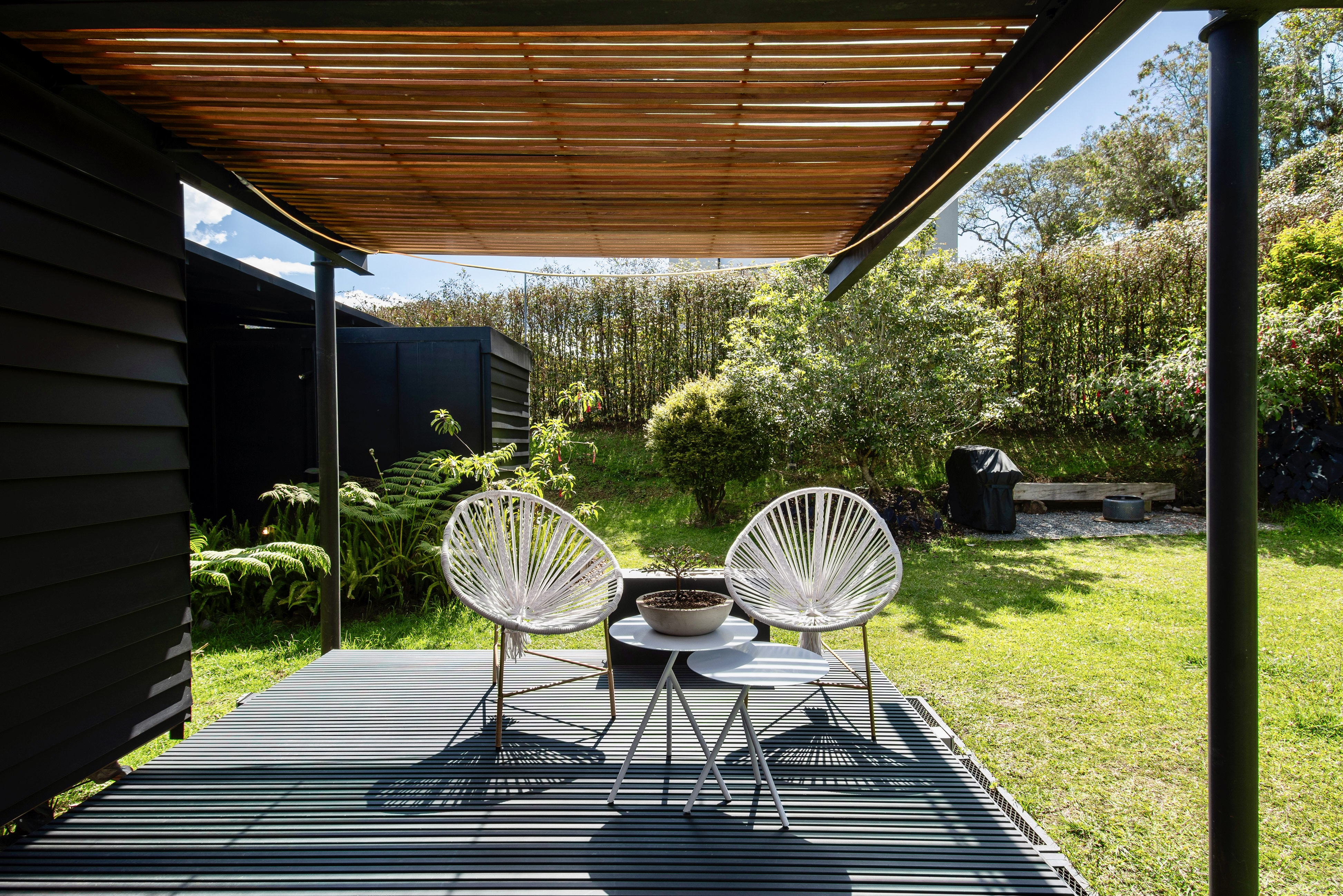 Covered deck with chairs facing a green garden slope